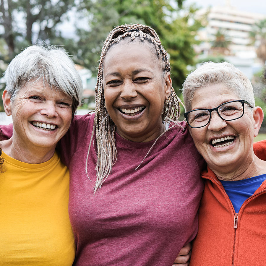 A group of older women of various races and ethnicities laughing with their arms around each other