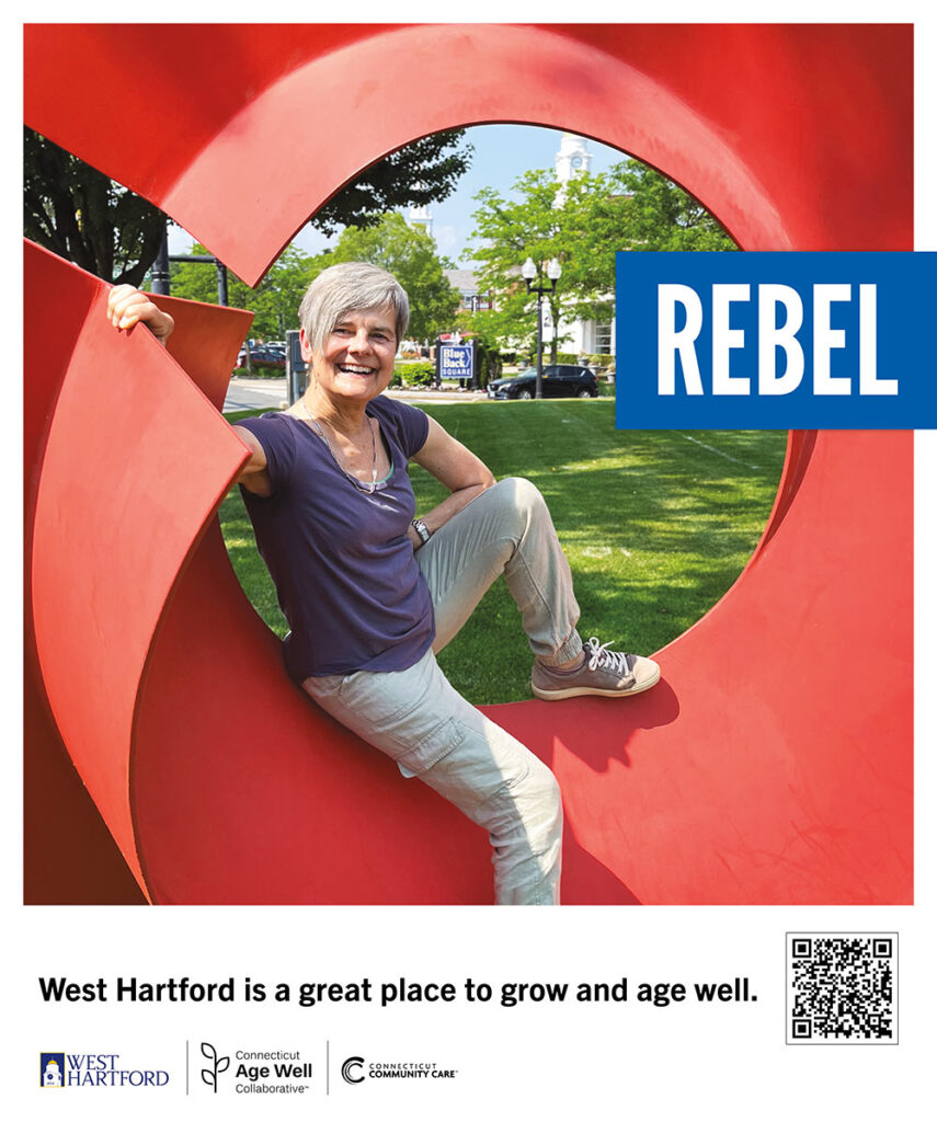 Diane sits on a monumental, abstract, red sculpture on the lawn of West Hartford town hall