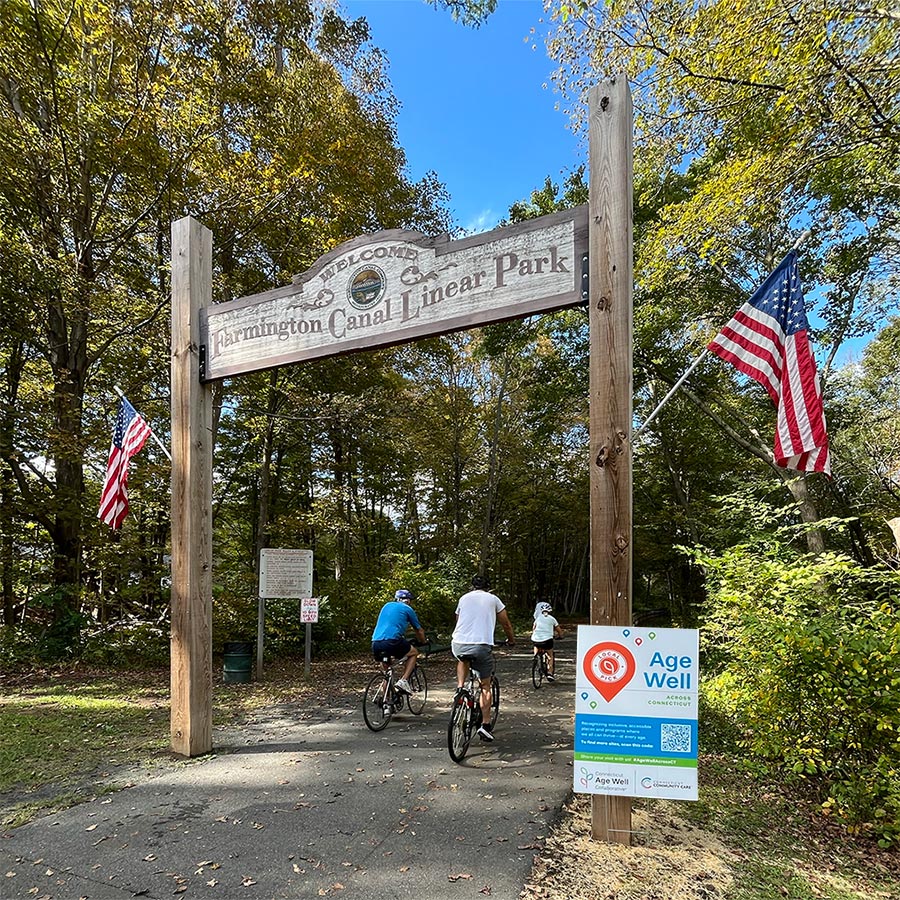 An entrance to the Farmington Canal Linear Park, with an Age Well Across Connecticut Local Pick sign prominently displayed